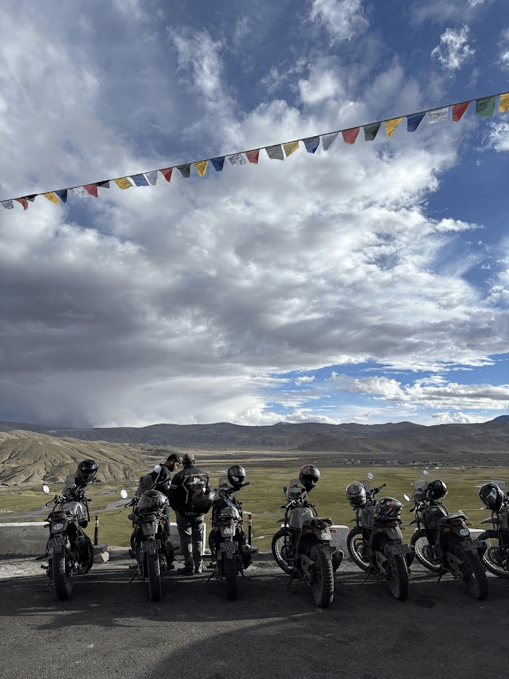 Seven adventure motorcycles lined up on a high-altitude pass overlooking a green valley